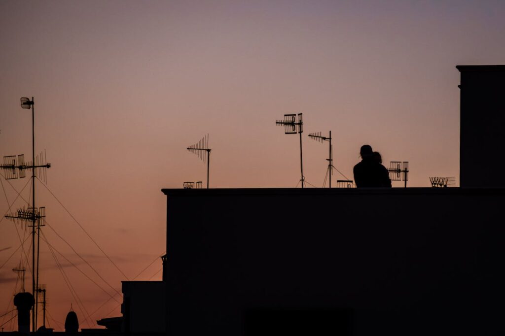 Silhouette of a couple embracing on a rooftop with TV antennas at sunset. City romance captured.
